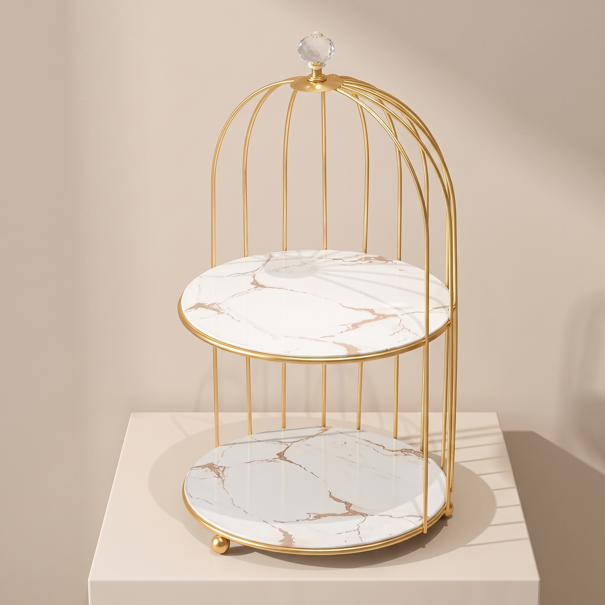 A two-tier decorative stand with a gold metal cage frame and white marble-patterned trays, displayed on a beige pedestal against a neutral beige background.