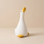 A white goose-shaped night light with a yellow beak, black eye, and yellow feet, sitting on a beige surface against a matching beige background.