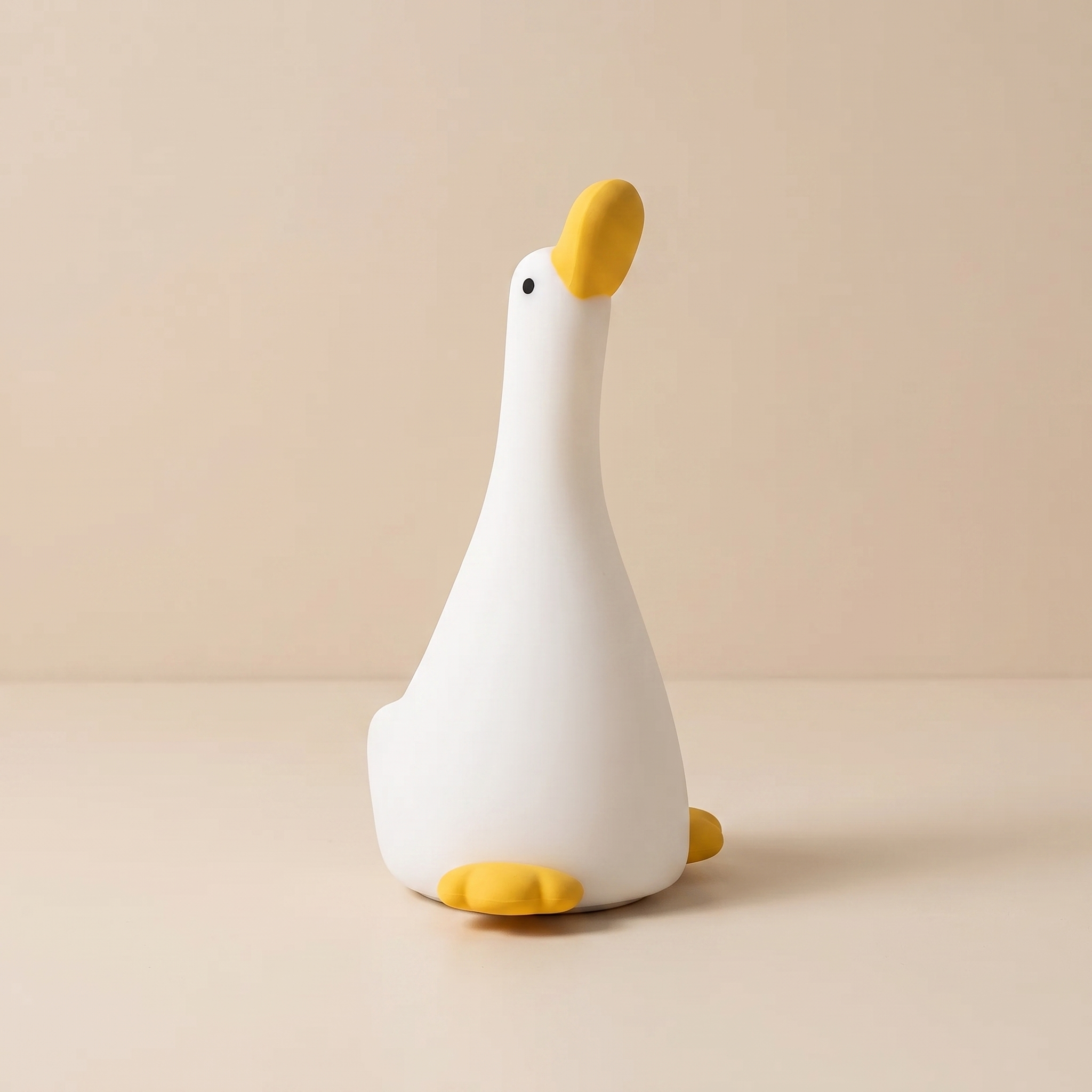 A white goose-shaped night light with a yellow beak, black eye, and yellow feet, sitting on a beige surface against a matching beige background.