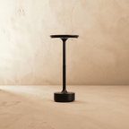 A modern black metal pedestal table with a circular top and round base, set against a textured beige plaster wall and floor.