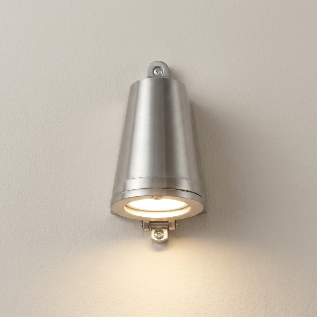 A modern wall-mounted cone-shaped light fixture with a brushed silver metal finish, shown illuminated against a plain off-white wall.