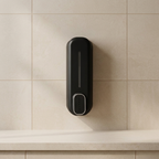 A matte black wall-mounted dispenser, likely for soap or lotion, mounted on a beige tiled wall above a light countertop.