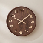 A round wooden wall clock with a dark brown wood grain face and light beige numerals and hands, mounted on a plain off-white wall.
