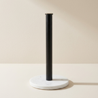 A modern paper towel bar with a matte black cylindrical pole and a round white marble base, set against a warm beige background.