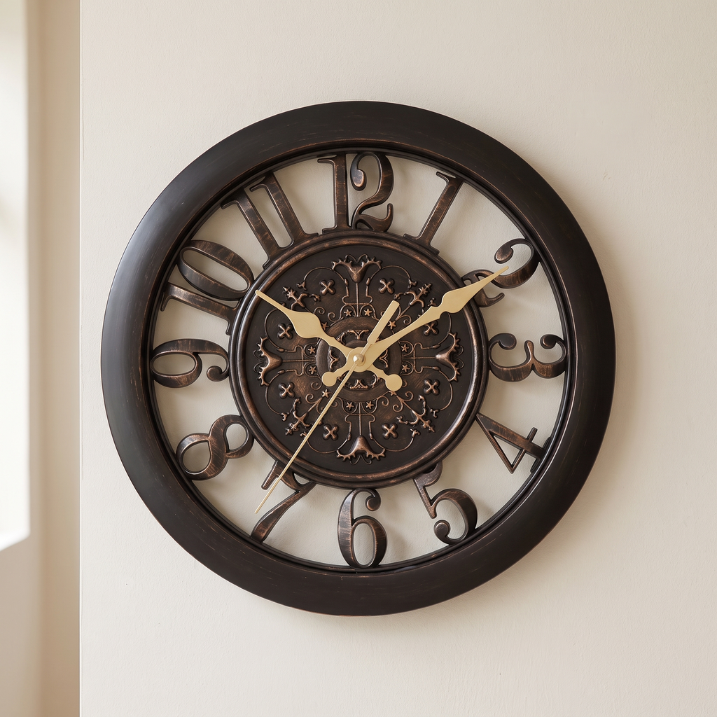 A large round wall clock with a dark brown frame and ornate cutout numerals, featuring gold-tone hands and a decorative central medallion, mounted on a light beige wall.