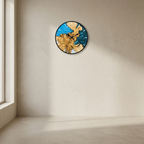 A round wall clock with an abstract map design in blue and gold tones, mounted on a beige plaster wall next to a window.