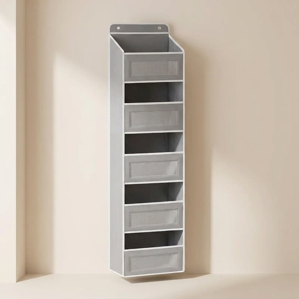 A tall, narrow gray wall-mounted organizer with six open shelves and four front drawer compartments, shown against a warm beige wall.
