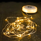 Warm white solar fairy string lights coiled on a dark textured surface, with a small solar panel visible in the background.