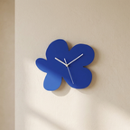 A modern blue flower-shaped wall clock with white hands, mounted on a warm beige textured wall.