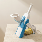 A kitchen mandoline slicer with a white and blue plastic body, shown standing on a light stone countertop with sliced lemons in a clear collection tray.