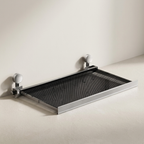 A modern wall-mounted retractable mesh shelf with a silver metal frame and white spherical wall mounts, shown partially extended against a minimalist off-white wall and floor.