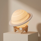 A planet-shaped night light resembling Saturn, made from a warm-toned wood grain material, resting on a small wooden stand atop a white pedestal against a beige background.