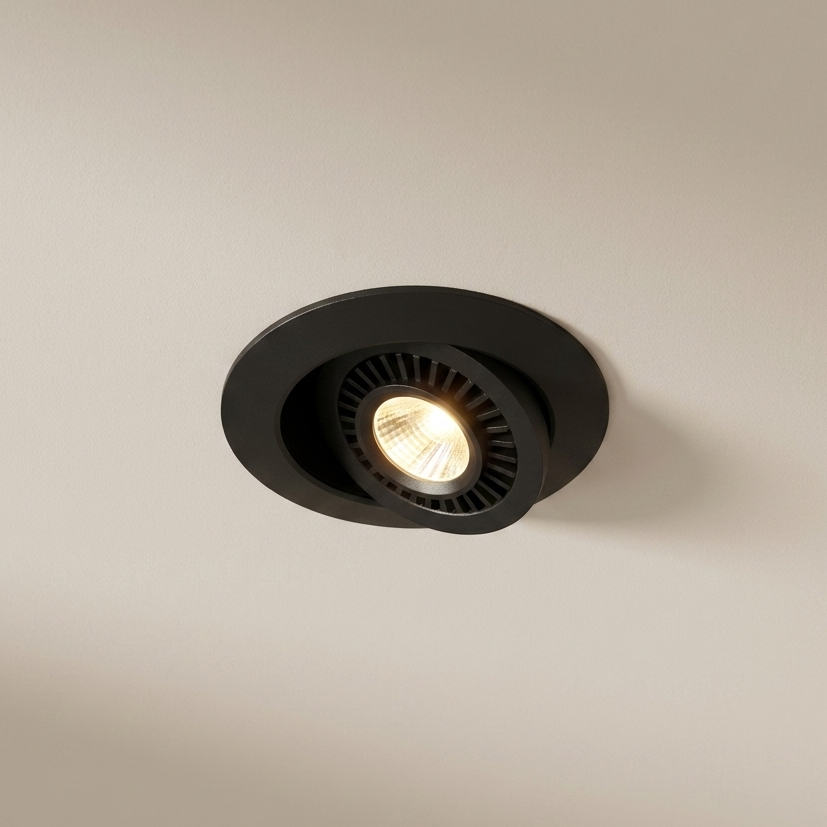 A round black recessed spotlight ceiling light fixture emitting a warm yellow glow, shown against a plain beige wall.
