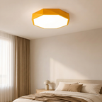 A modern geometric octagonal ceiling light in a warm yellow-orange color, glowing with a bright white light in a minimalist beige bedroom.