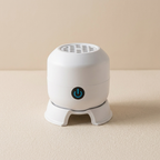 A small white cylindrical electronic device with a power button icon on the front, standing on a matching white base against a warm beige background.