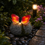 A garden light sculpture shaped like a butterfly perched on a mossy stone, glowing warmly in a rainy outdoor garden setting with wet pebbles and plants.