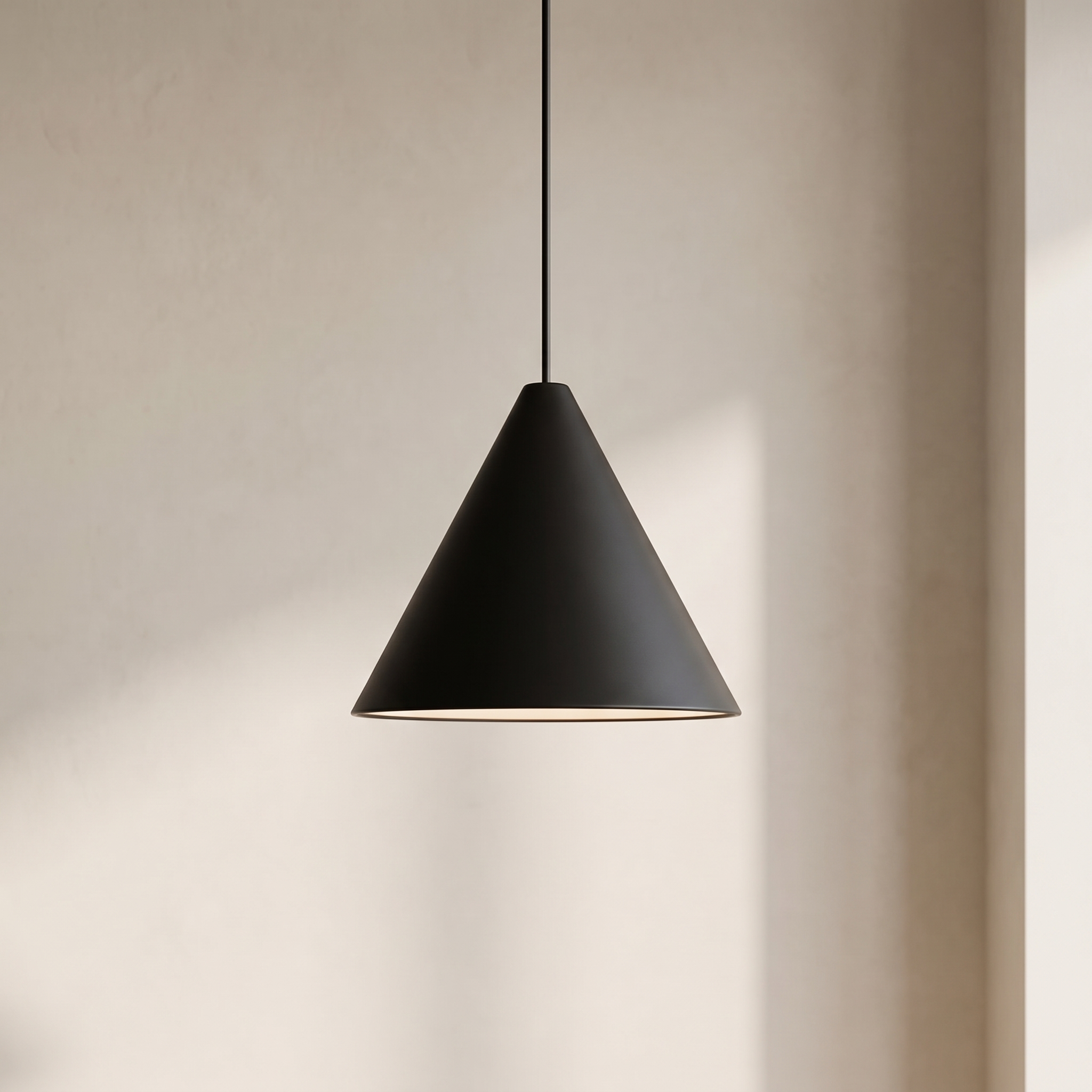 A matte black cone-shaped pendant light hanging from a thin black cord against a warm beige plaster wall, casting a soft shadow to the right.