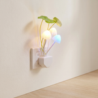 A wall-plugged night light shaped like a small plant with glowing mushroom-shaped bulbs in white, warm yellow, and blue, set against a beige wall and light wood floor.