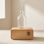 A wooden diffuser base with a clear glass bottle on top, emitting a visible plume of steam, set against a softly lit beige background.