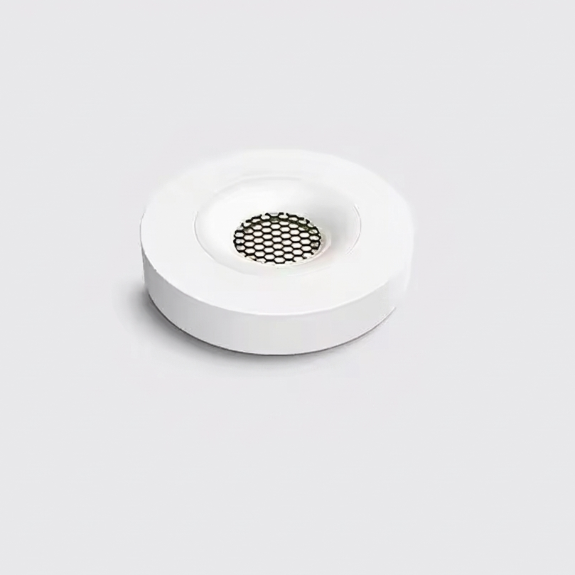 A minimalist white circular tray or shallow dish with a small black mesh center, photographed on a clean light gray background.