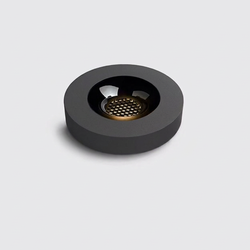 A minimalist round black ashtray with a textured metallic gold center, shown on a solid light gray background.