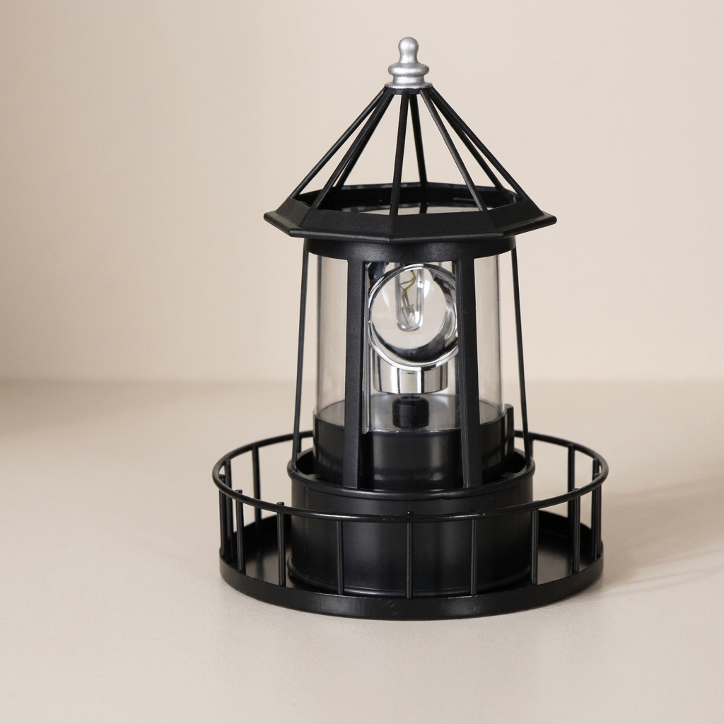 A black metal nautical lighthouse table lamp with a clear glass shade and a silver-toned light bulb visible inside, set against a plain beige background.