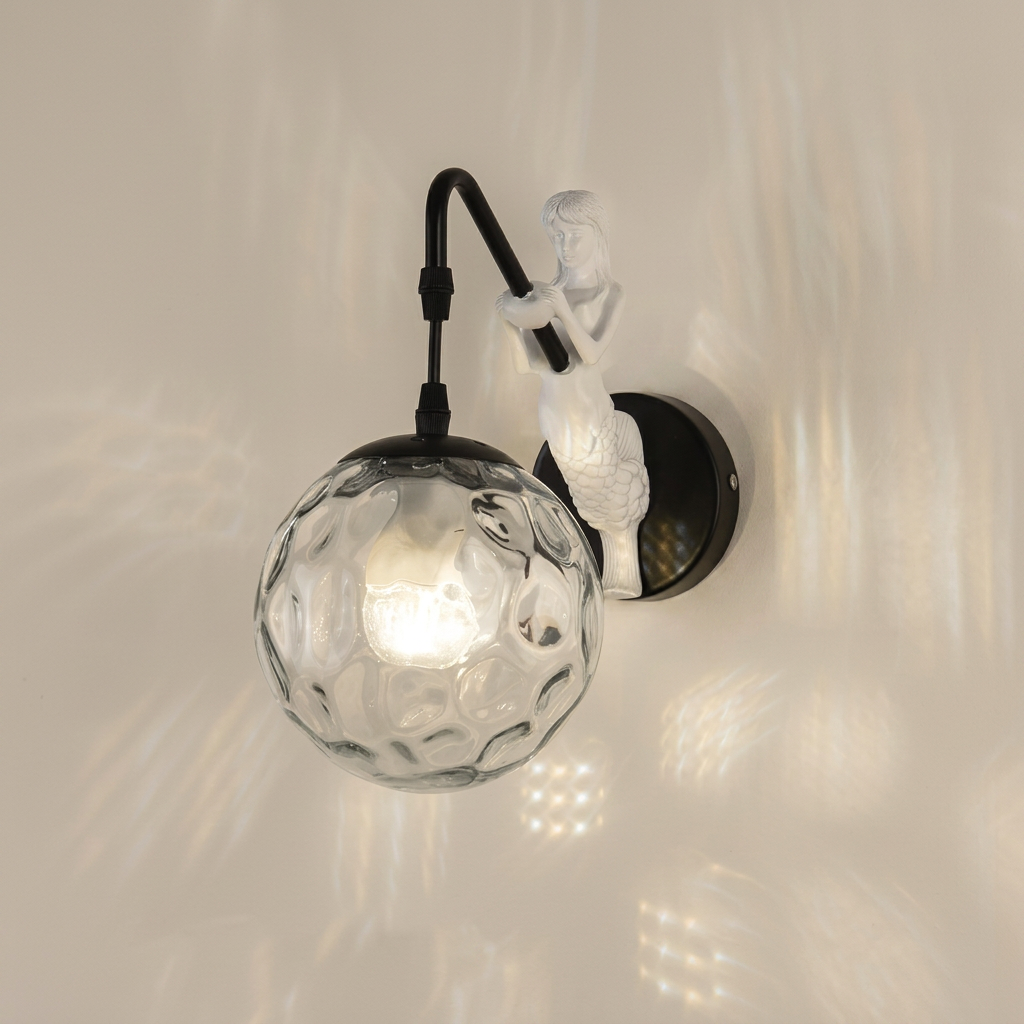 A wall-mounted light fixture with a black curved arm, a white sculptural figure, and a textured clear glass globe shade, shown lit against a warm off-white wall.