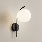 Modern wall sconce with a matte black curved metal frame and a large frosted white globe shade, mounted on a light beige wall.