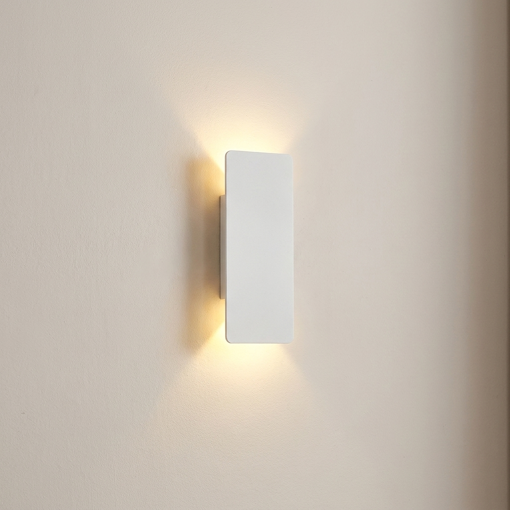 A minimalist rectangular wall sconce light fixture in matte white, mounted on a warm beige wall and casting a soft warm yellow glow downward and outward.