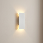 A minimalist rectangular wall sconce light fixture in matte white, mounted on a warm beige wall and casting a soft warm yellow glow downward and outward.