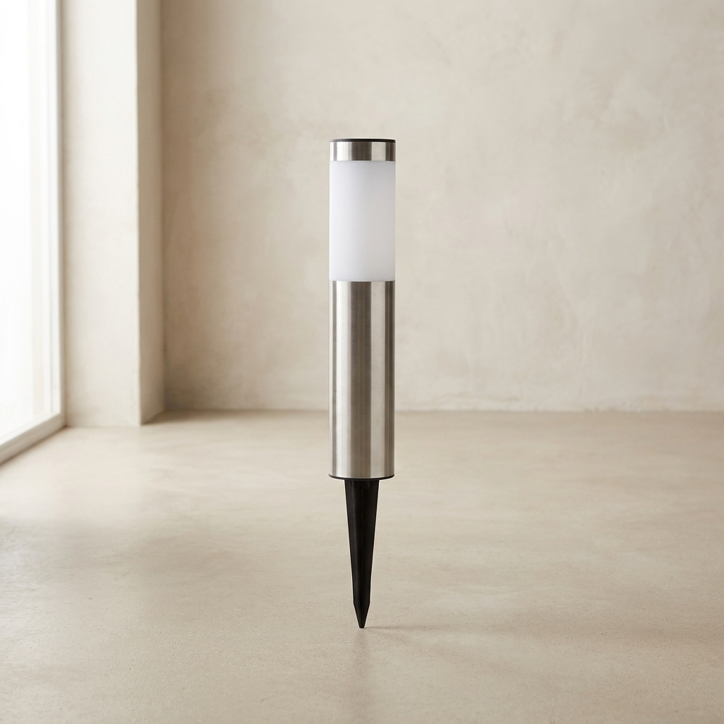 A modern solar outdoor ground stake light with a brushed silver metal body, a frosted white cylindrical light-up section, and a black ground spike, shown standing on a concrete floor against a textured beige wall.