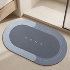 An oval-shaped gray and light blue bathroom floor mat with the word 'HOME' printed in the center, shown on a beige tiled floor near a bathtub.
