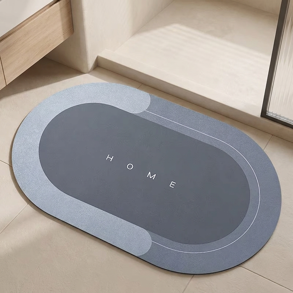 An oval-shaped gray and light blue bathroom floor mat with the word 'HOME' printed in the center, shown on a beige tiled floor near a bathtub.