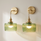 A pair of wall-mounted sconces with ribbed translucent green glass shades and brushed brass hardware, shown lit against a plain off-white wall.