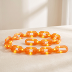 A translucent orange plastic link chain, illuminated with warm yellow lights, coiled on a light beige fabric surface.