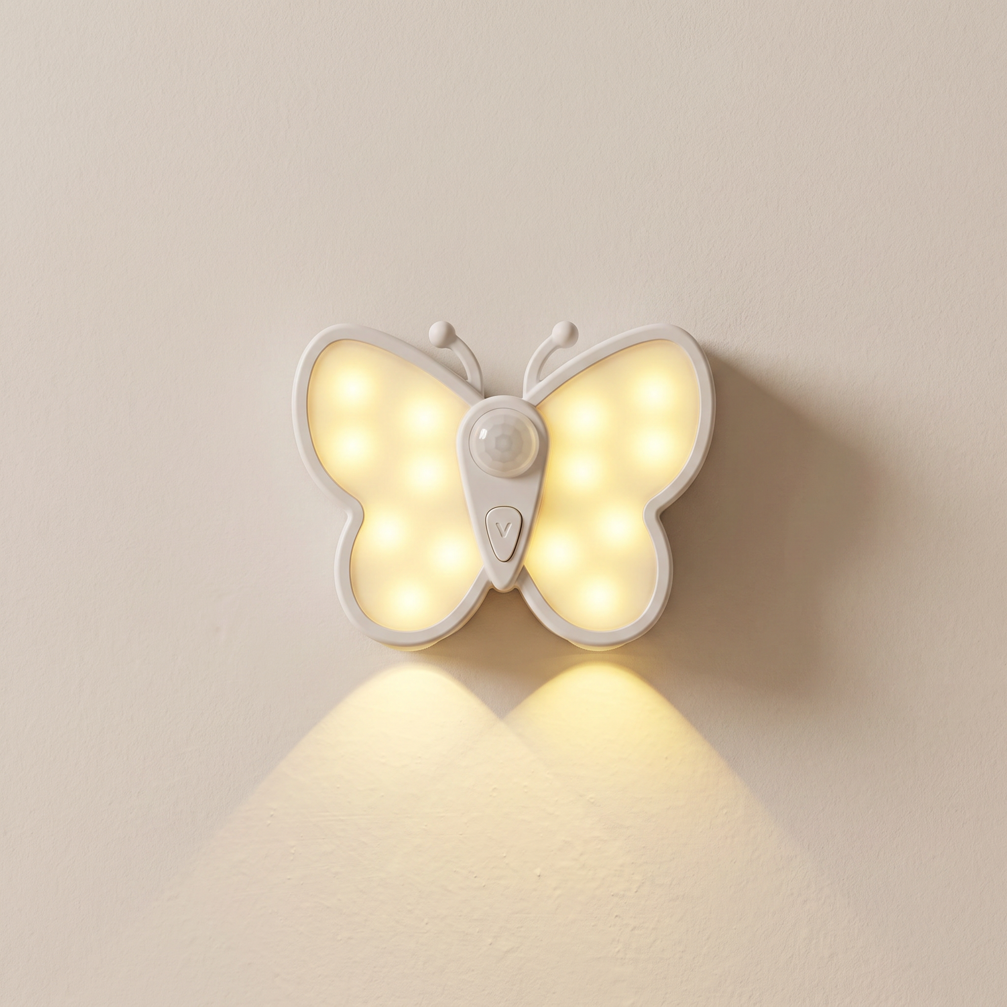 A butterfly-shaped wall night light with glowing warm white LED lights, mounted on a plain beige wall. The light has a white plastic body with a central sensor and casts a soft glow downward.