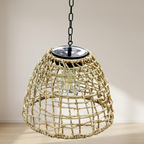 A natural woven rattan pendant light in a conical dome shape, suspended by a black metal chain with a solar panel on top, set against a neutral beige wall and light wood floor.