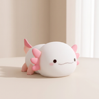 A cute, small white axolotl-shaped plush toy or lamp with pink gills and legs, resting on a light beige surface in a softly lit indoor setting.