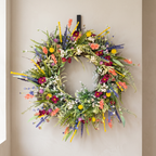 A vibrant, multicolored wildflower wreath hanging on a neutral beige wall.