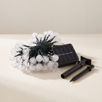 Solar string lights with clear faceted round bulbs, a small black solar panel, and two black ground stakes on a light beige surface.