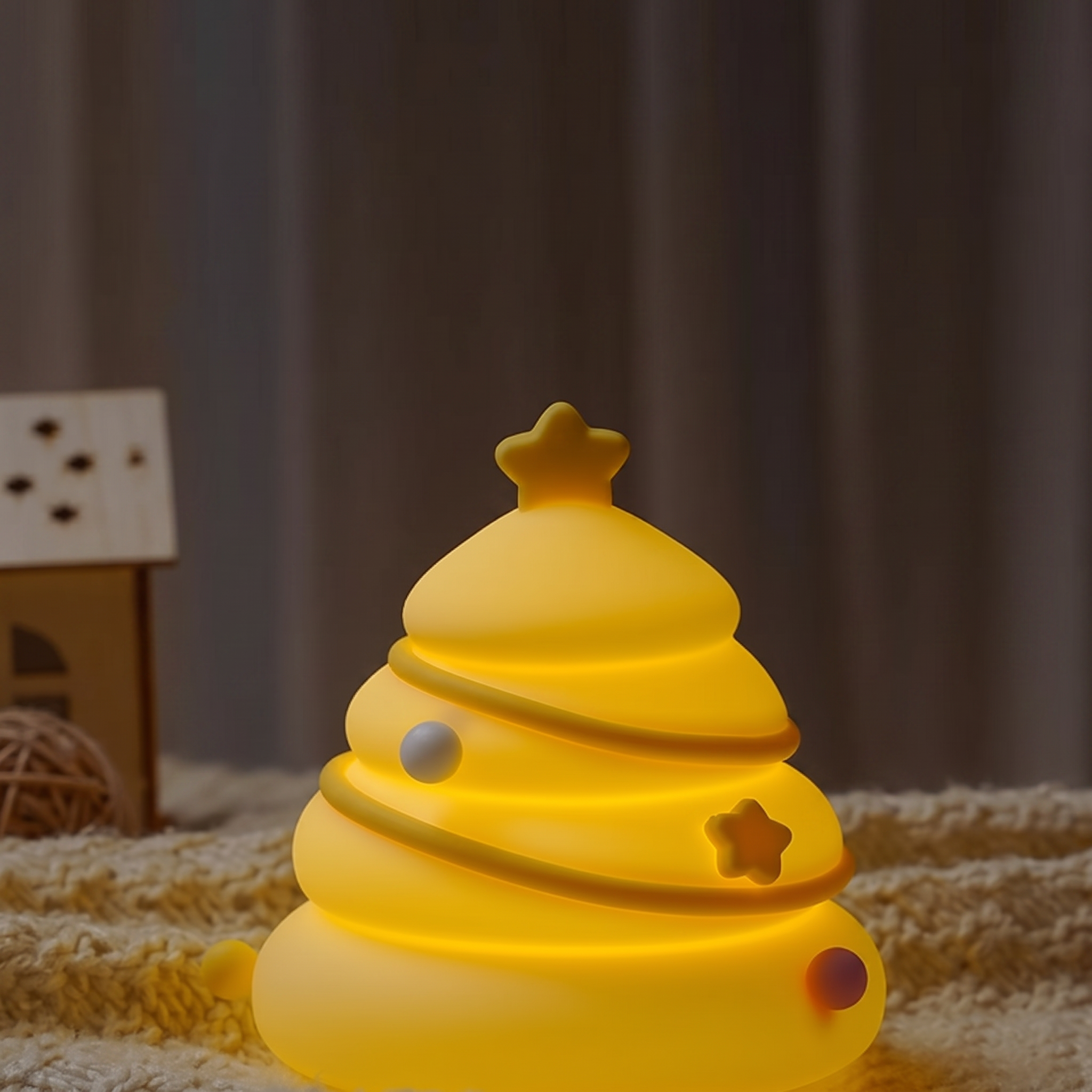A glowing yellow Christmas tree shaped night light with star and round ornament details, placed on a textured cream blanket with a soft-focus indoor background.