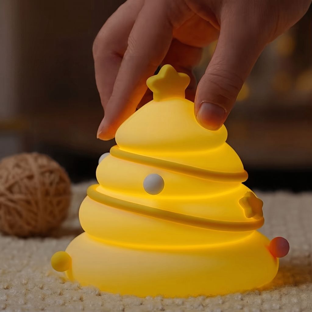 A hand is turning on a glowing yellow Christmas tree-shaped night light, placed on a textured beige surface with a warm, blurred background.