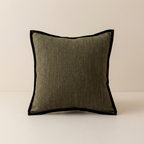 A square throw pillow with an olive green linen-textured center and a contrasting black velvet border, set against a neutral cream background.