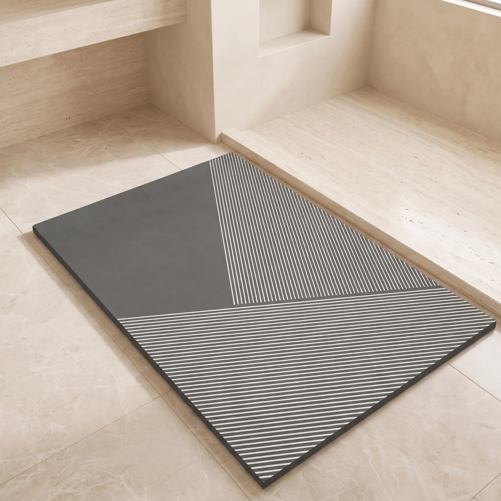 A rectangular gray mat with a geometric pattern of solid dark gray and white diagonal stripes, placed on a light beige stone floor in a minimalist interior setting.