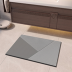A rectangular gray bath mat with a geometric pattern of solid gray and black-and-white striped sections, placed on a light beige tiled bathroom floor in front of a dark wood vanity.