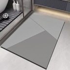 A rectangular bathroom floor mat with a modern geometric design, featuring a solid gray lower section and diagonal striped sections in white and gray. The mat is shown in a clean, contemporary bathroom setting.