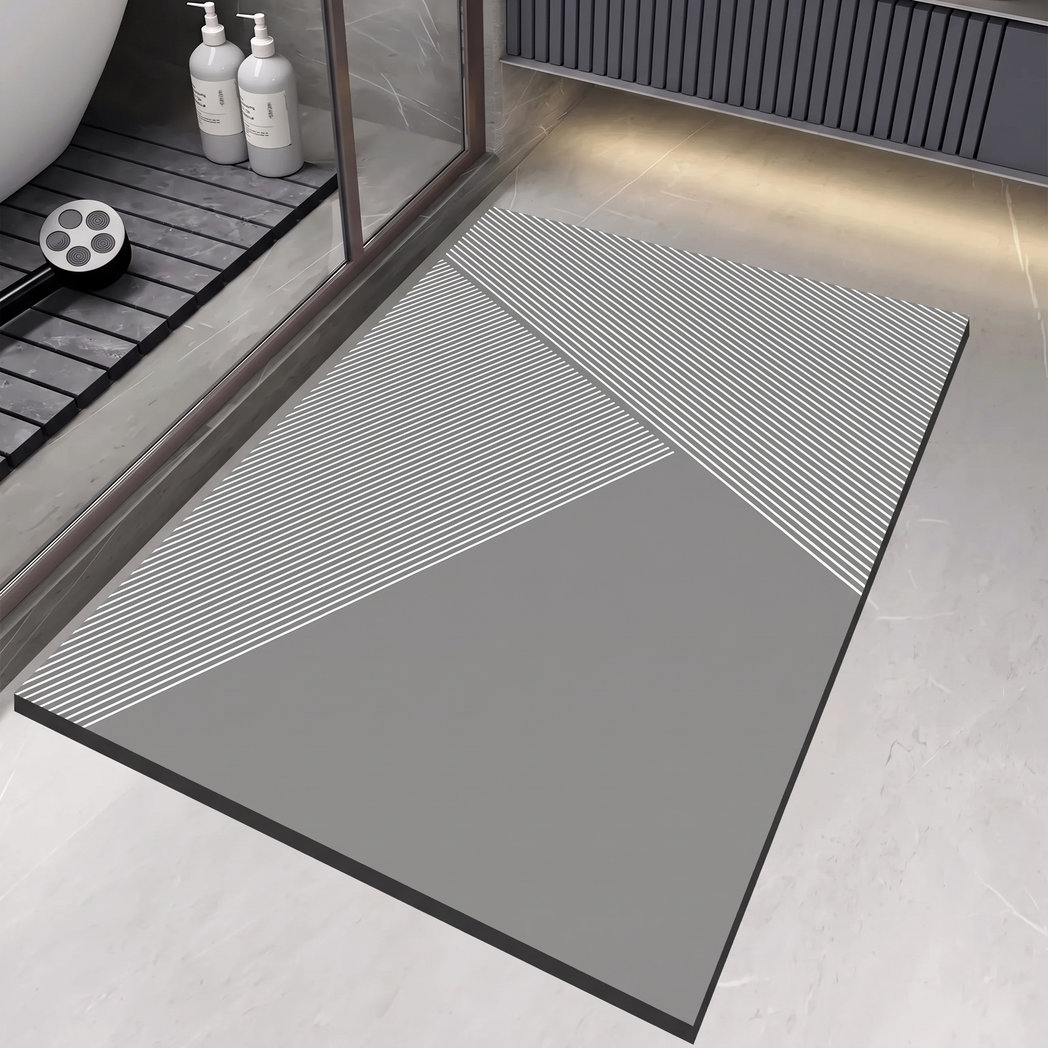 A rectangular bathroom floor mat with a modern geometric design, featuring a solid gray lower section and diagonal striped sections in white and gray. The mat is shown in a clean, contemporary bathroom setting.