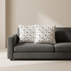 Two white textured throw pillows with black embroidered eyes and mouths, styled on a modern gray fabric sofa against a warm beige wall.