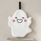 A white plush ghost-shaped bath sponge with embroidered black facial features, pink cheeks, and a black hanging loop, displayed against a neutral beige wall.