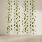 Green wall hanging with warm white string lights, suspended in vertical strands against a plain beige wall and light floor.